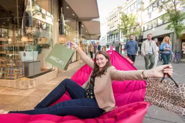 Frau mit Einkaufstüten sitzt auf Fatboy-Stuhl und streckt die Arme aus