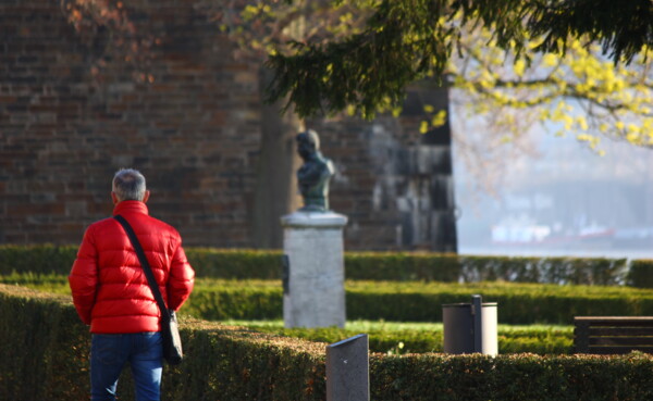 Mann mit roter Jacke steht in den Rheinanlagen am Rhein © 