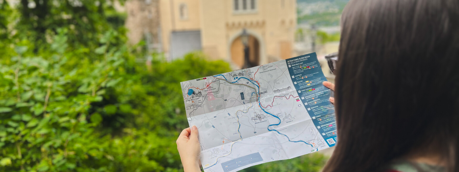 Frau steht vor Schloss Stolzenfels und blickt auf einer Broschüre © Ryne & Denise Cook