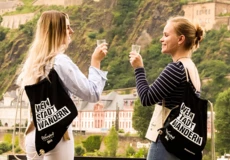 Zwei Mädels sitzen auf einer Mauer mit einer Flasche Wein und schauen ihre WeinStadtWander-Route auf einer Karte an. © Koblenz-Touristik, Johannes Bruchhof