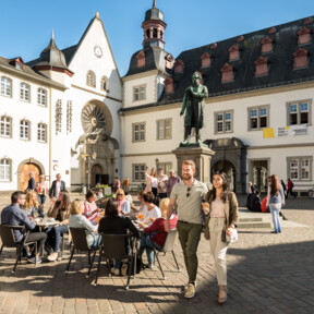 © Koblenz-Touristik GmbH, Dominik Ketz Pärchen im Vordergrund spaziert und Menschengruppen im Hintergrund sitzen an Cafétischen auf dem Jesuitenplatz in der Koblenzer Altstadt © Koblenz-Touristik GmbH, Dominik Ketz