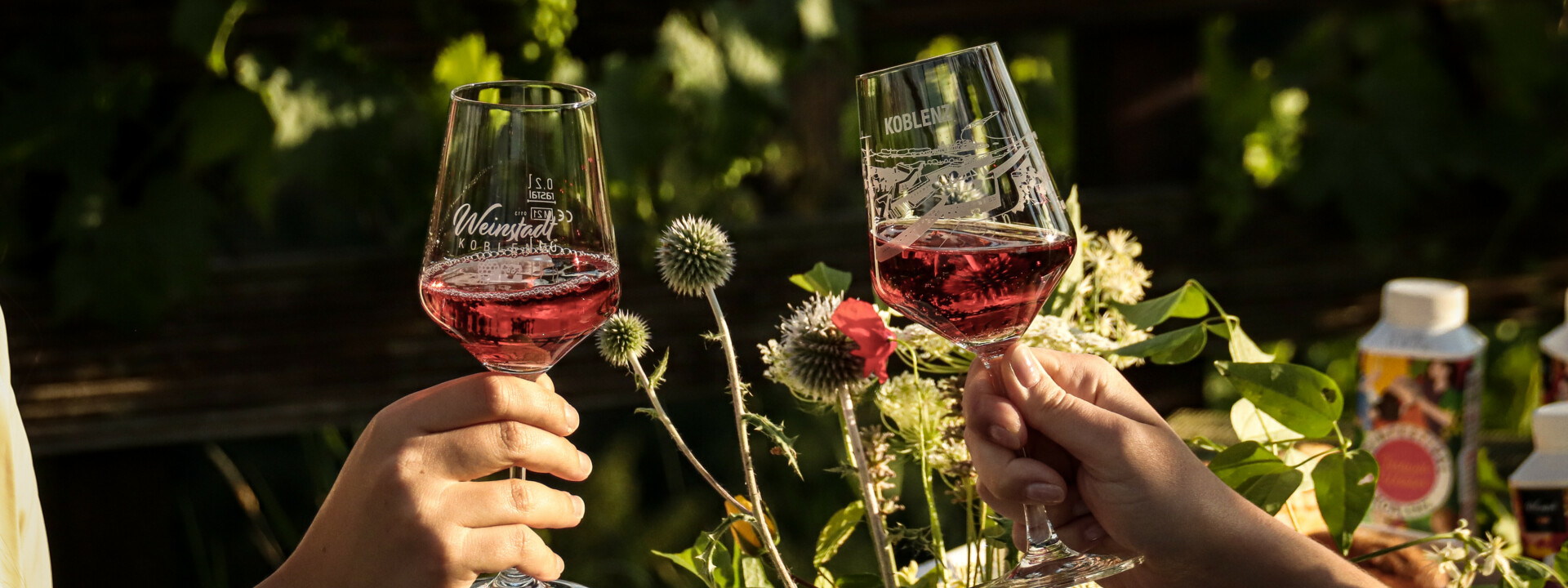 Zwei Personen stoßen mit Koblenz-Weingläsern an, mit schön gedecktem Tisch unter freiem Himmel im Hintergrund © Koblenz-Touristik GmbH, Johannes Bruchhof