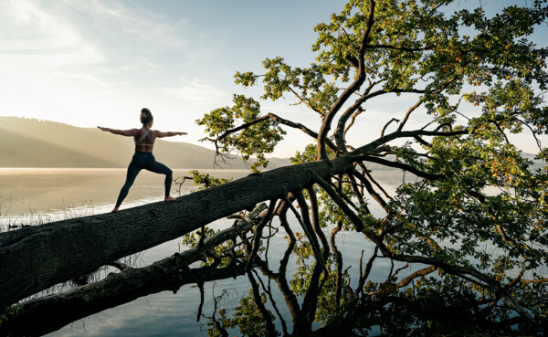 Dame in Kriegerstellung macht Yoga auf einem Baumstamm im Wasser beim Sonnenaufgang bei Maria Laach © Koblenz-Touristik GmbH, Philip Bruederle Dame in Kriegerstellung macht Yoga auf einem Baumstamm im Wasser beim Sonnenaufgang bei Maria Laach © Koblenz-Touristik GmbH, Philip Bruederle