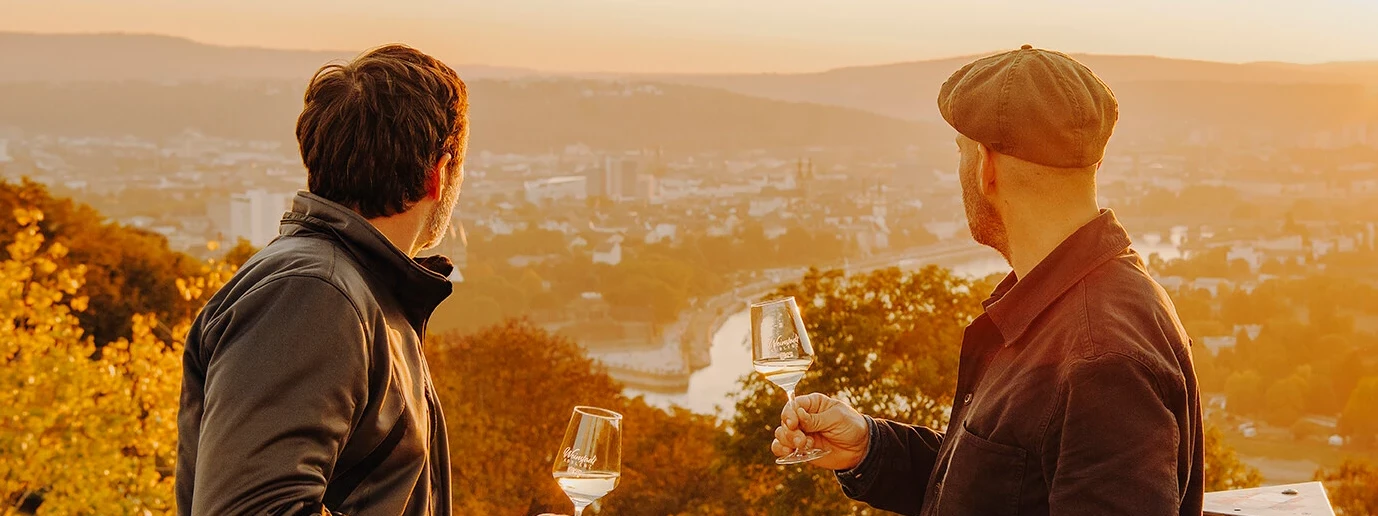 Männer Wein Aussichtsplattform Koblenz Sonnenuntergang © Koblenz-Touristik GmbH, Philip Bruederle Zwei Männer von der Seite halten Weingläser und blicken auf die Stadt Koblenz beim Sonnenuntergang © Koblenz-Touristik GmbH, Philip Bruederle