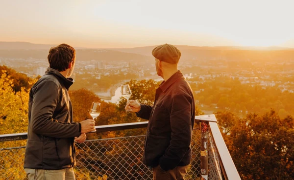 Männer Wein Aussichtsplattform Koblenz Sonnenuntergang © Koblenz-Touristik GmbH, Philip Bruederle Zwei Männer von der Seite halten Weingläser und blicken auf die Stadt Koblenz beim Sonnenuntergang © Koblenz-Touristik GmbH, Philip Bruederle