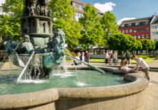 Brunnen Historiensäule Görresplatz Koblenz © Koblenz-Touristik GmbH, Dominik Ketz Brunnen "Historiensäule" auf dem Görresplatz in Koblenz umgeben von kleinen Menschengruppen © Koblenz-Touristik GmbH, Dominik Ketz
