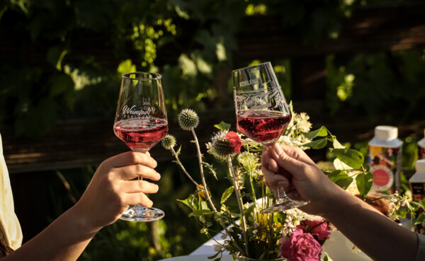 Anstoßen der Koblenz-Gläser © Koblenz-Touristik GmbH, Johannes Bruchhof Zwei Personen stoßen mit Koblenz-Weingläsern an, mit schön gedecktem Tisch unter freiem Himmel im Hintergrund © Koblenz-Touristik GmbH, Johannes Bruchhof