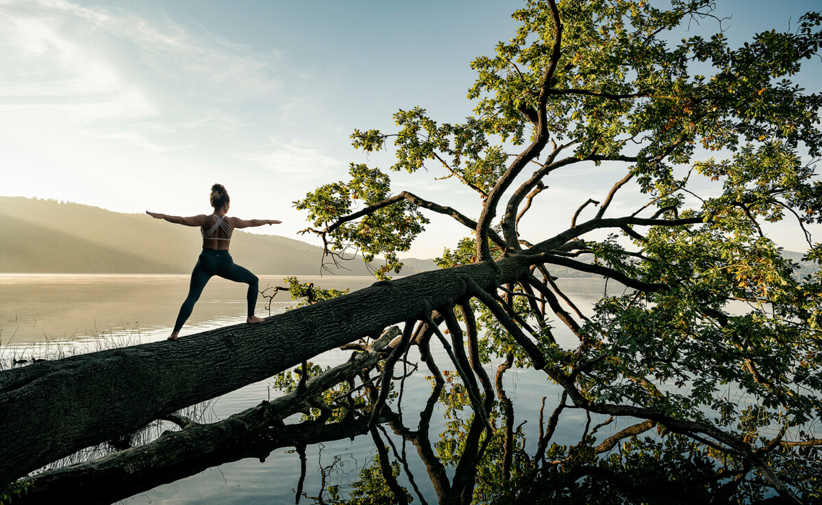 Frau Kriegerstellung Yoga Baum im Wasser Sonnenaufgang Maria Laach © Koblenz-Touristik GmbH, Philip Bruederle Dame in Kriegerstellung macht Yoga auf einem Baumstamm im Wasser beim Sonnenaufgang bei Maria Laach © Koblenz-Touristik GmbH, Philip Bruederle