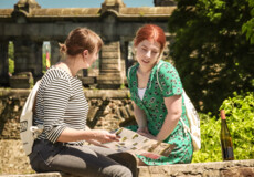Two girls sit on a wall with a bottle of wine and look at their WeinStadthiking route on a map. © Koblenz-Touristik GmbH, Johannes Bruchhof