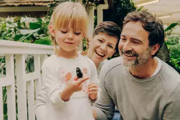 Familie im Schmetterlingsgarten in Sayn lachen während Tochter einen Schmetterling auf ihrem Finger beobachtet