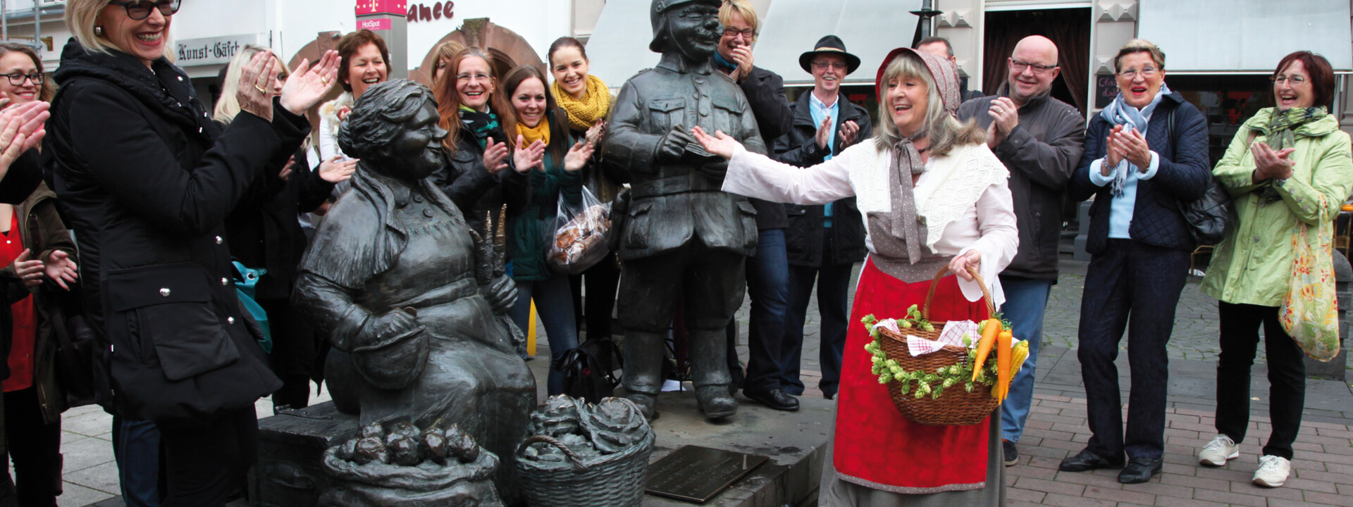 Verkleidete Stadtführerin mit Korb und Gemüse lacht mit einer Führungsgruppe vor Figuren auf dem Münzplatz © Koblenz-Touristik GmbH, Juraschek Verkleidete Stadtführerin mit Korb und Gemüse lacht mit einer Führungsgruppe vor Figuren auf dem Münzplatz © Koblenz-Touristik GmbH, Juraschek