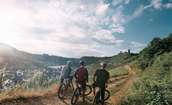 © Philip Bruederle Freundesgruppe auf Mountainbikes auf einem Radweg neben der Mosel mit Burg Thurant im Hintergrund © Philip Bruederle