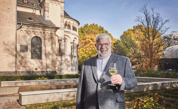 Lächelnder Stadtführer mit einem Glas Wein in der Hand steht vor dem Basilika St. Kastor im Herbst © Koblenz-Touristik GmbH, Picture Colada