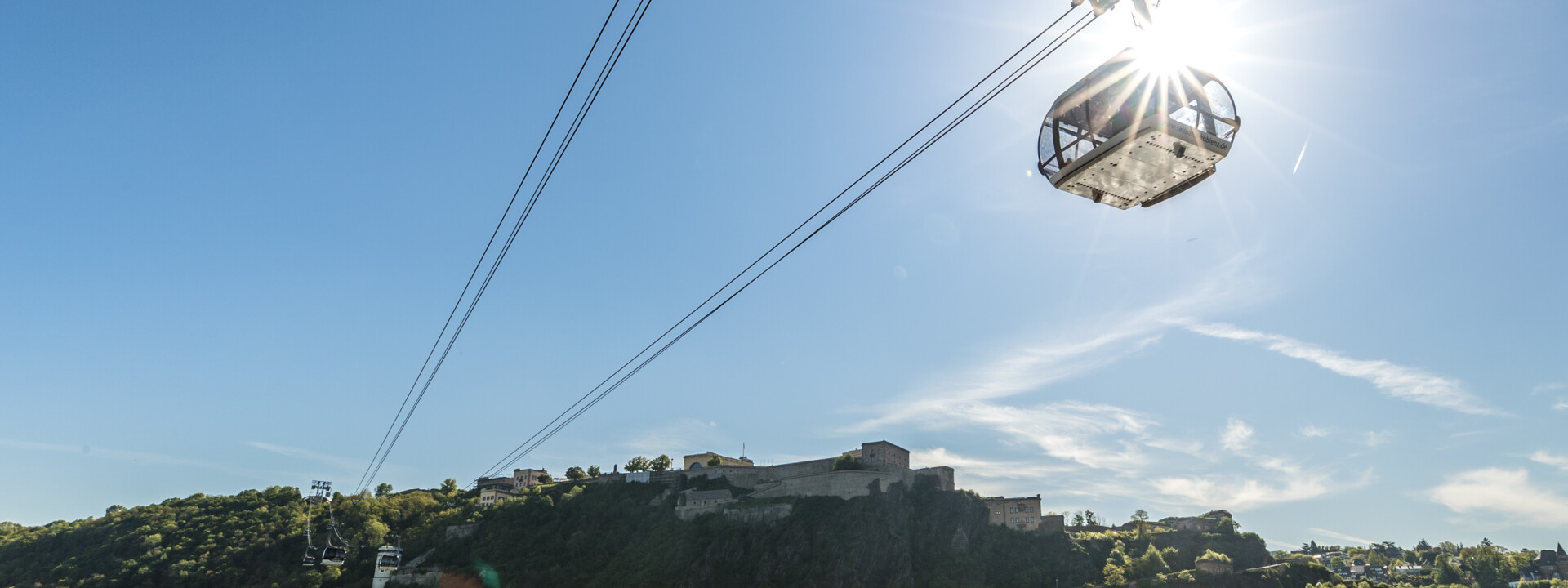 Die Seilbahn Koblenz hinterbeleuchtet von der Sonne mit Rhein im Vordergrund und Festung Ehrenbreitstein im Hintergrund © Koblenz-Touristik GmbH, Dominik Ketz