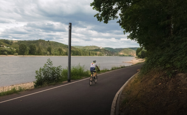 © Ryne & Denise Cook Rennradfahrer auf dem Rheinradweg mit dem Rhein und der Marksburg im Hintergrund © Ryne & Denise Cook