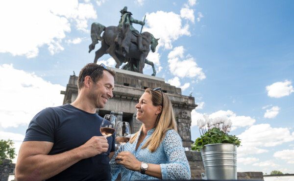 © Koblenz-Touristik GmbH, Dominik Ketz Pärchen steht mit Weinglas in der Hand vor dem Kaiser Wilhelm Denkmal am deutschen Eck und lachen sich gegenseitig an © Koblenz-Touristik GmbH, Dominik Ketz